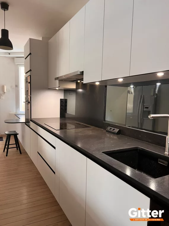 Cuisine parallèle, façades blanches sans poignées, plan de travail foncé et crédence miroir, réalisation Gitter à Hagondange