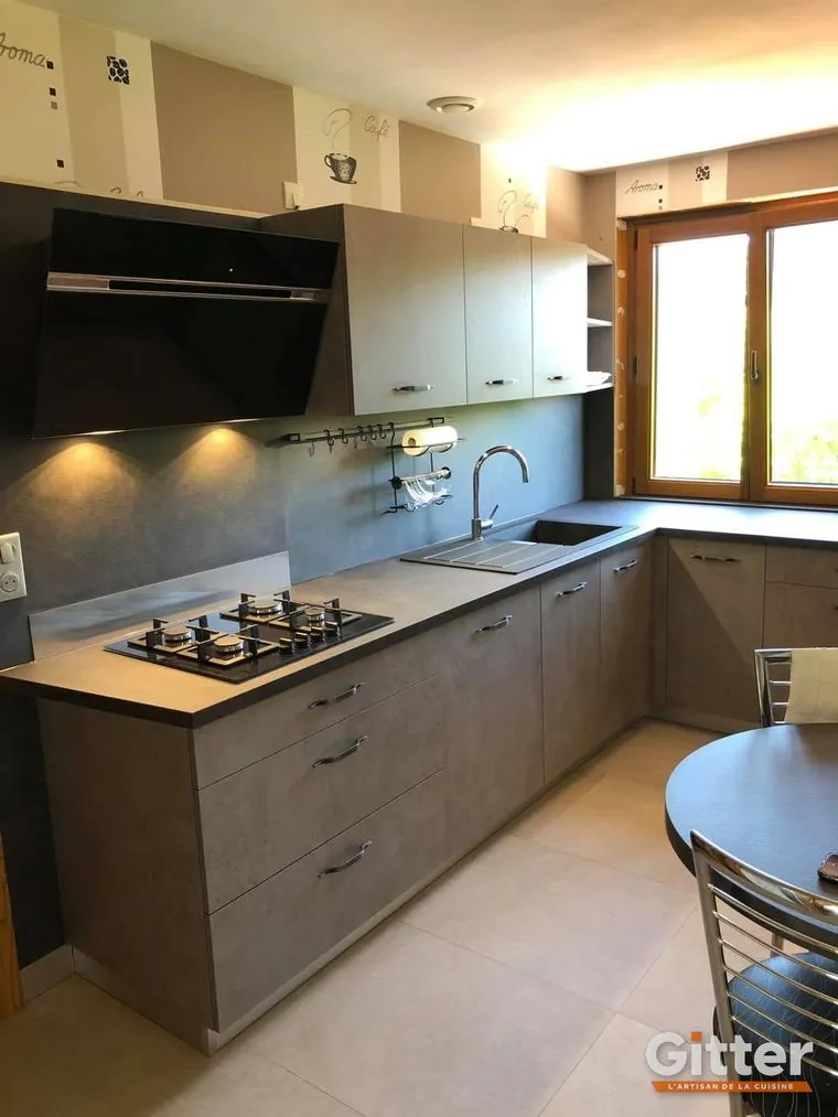 Cuisine en L, façades taupe, crédence noire, hotte décorative et table ronde, réalisation Gitter à Bousse