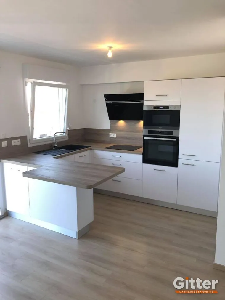 Cuisine ouverte avec îlot, façades blanches mates et plan de travail bois sur parquet, réalisation Gitter à Serémange-Erzange