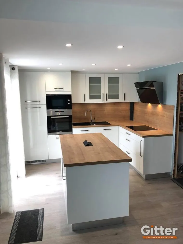 Cuisine avec îlot, façades blanches, plan de travail bois et hotte inclinée noire, réalisation Gitter à Nancy