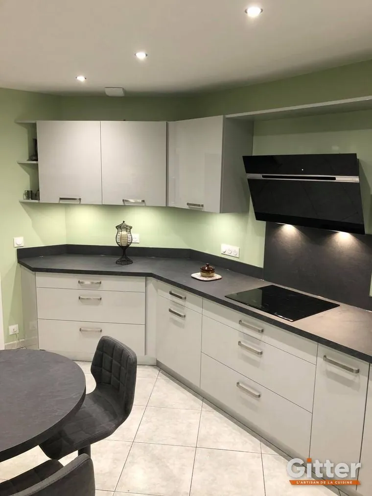 Cuisine en L, façades blanches, plan de travail foncé et hotte inclinée noire, réalisation Gitter à Clouange