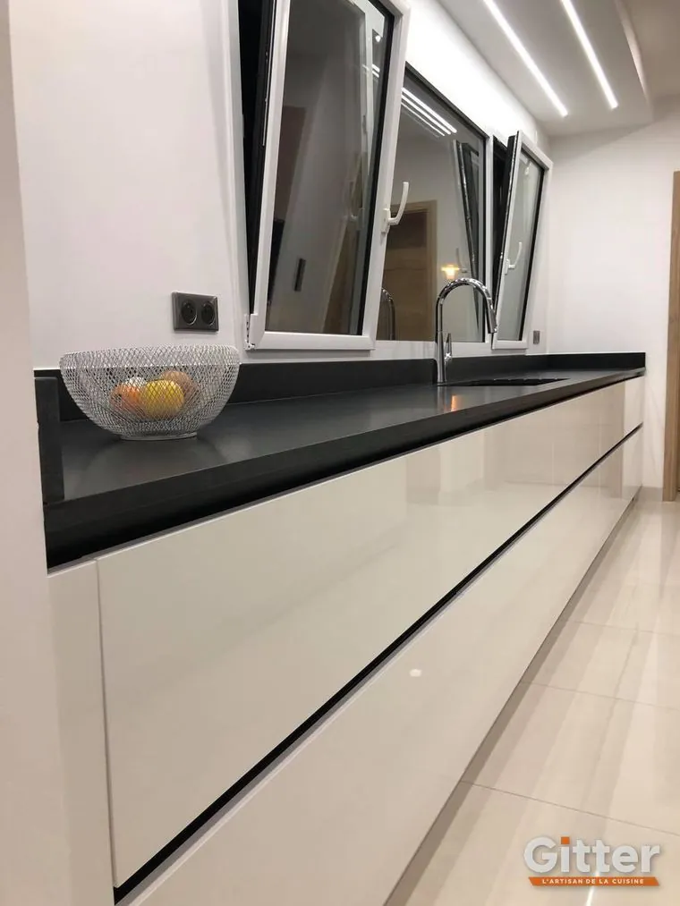 Cuisine : plan de travail noir et façades blanches brillantes sans poignées, sous fenêtre bandeau, réalisation Gitter à Saint-Julien-lès-Metz