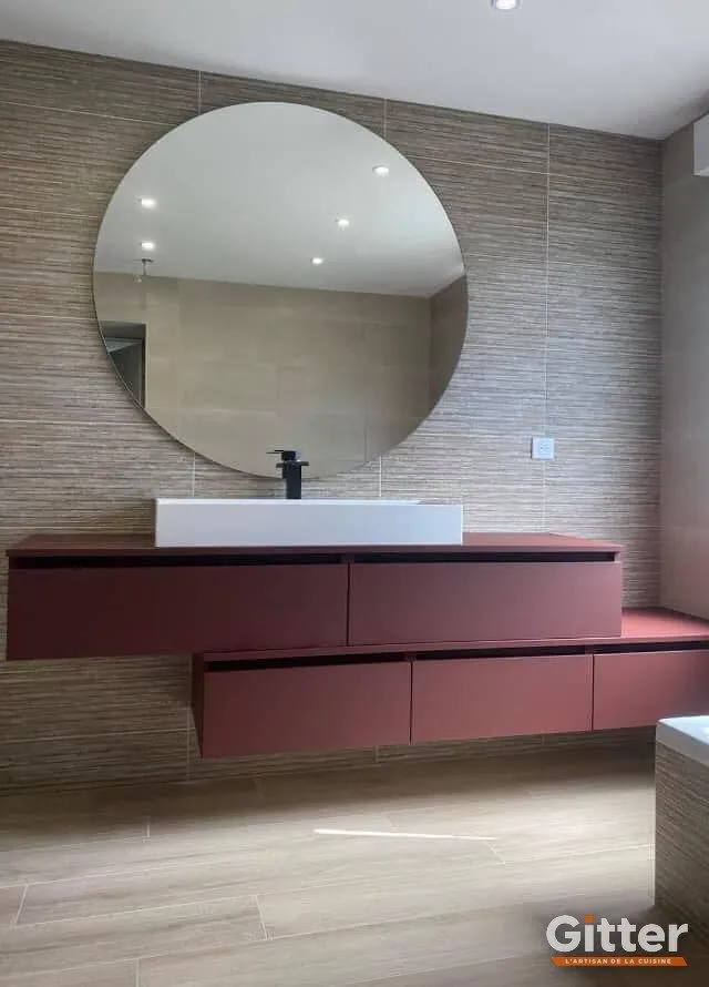 Salle de bains : meuble suspendu bordeaux, vasque à poser et miroir rond, réalisation Gitter à Manom