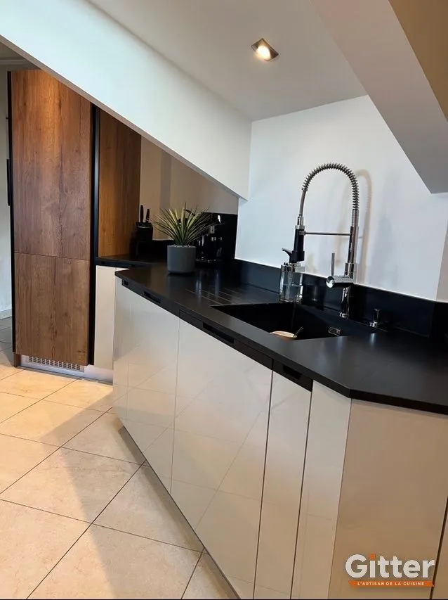 Cuisine sous pente, façades claires, plan de travail noir et colonne bois, réalisation Gitter à Basse-Ham