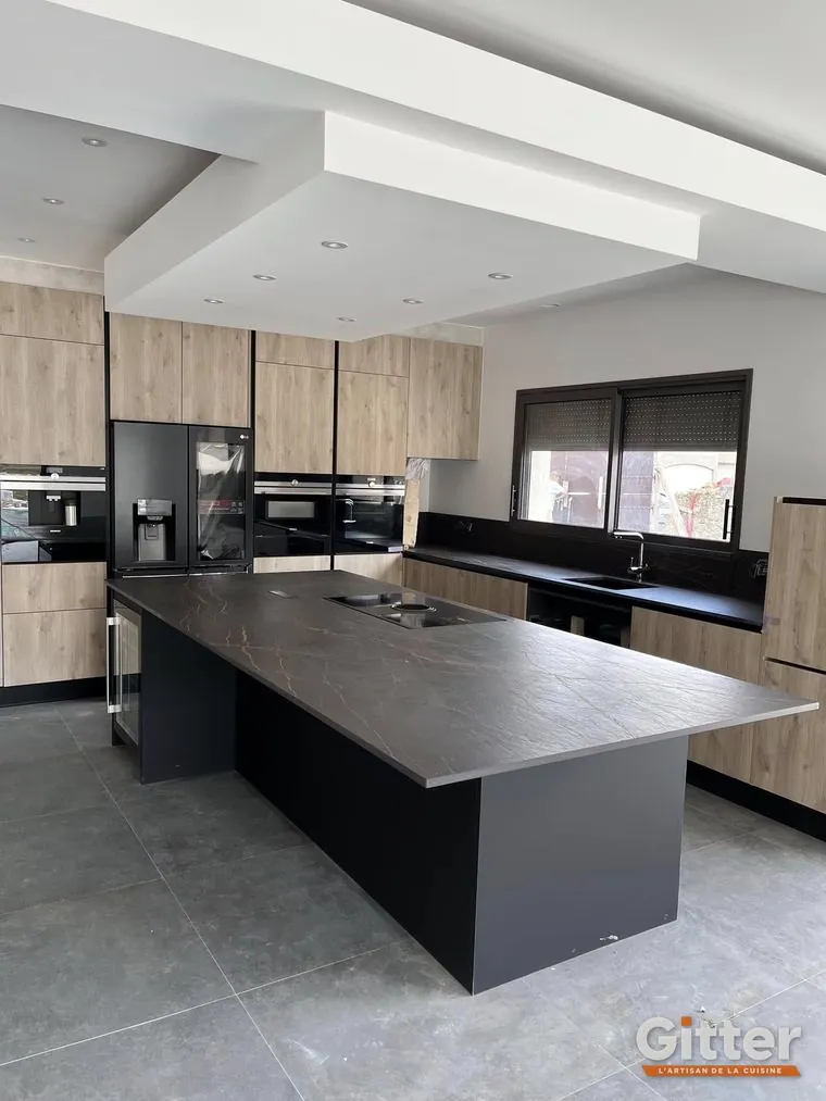 Cuisine : grand îlot noir, façades bois et colonnes four, réalisation Gitter à Pont-à-Mousson