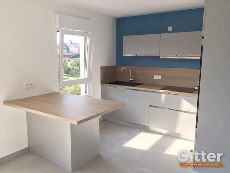 Cuisine : façades claires et table centrale bois sur mur bleu, réalisation Gitter à Richemont