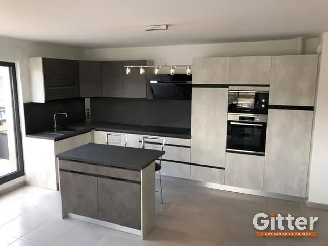 Cuisine en U avec îlot, façades effet béton, plan de travail noir et colonnes four, réalisation Gitter à Mondelange