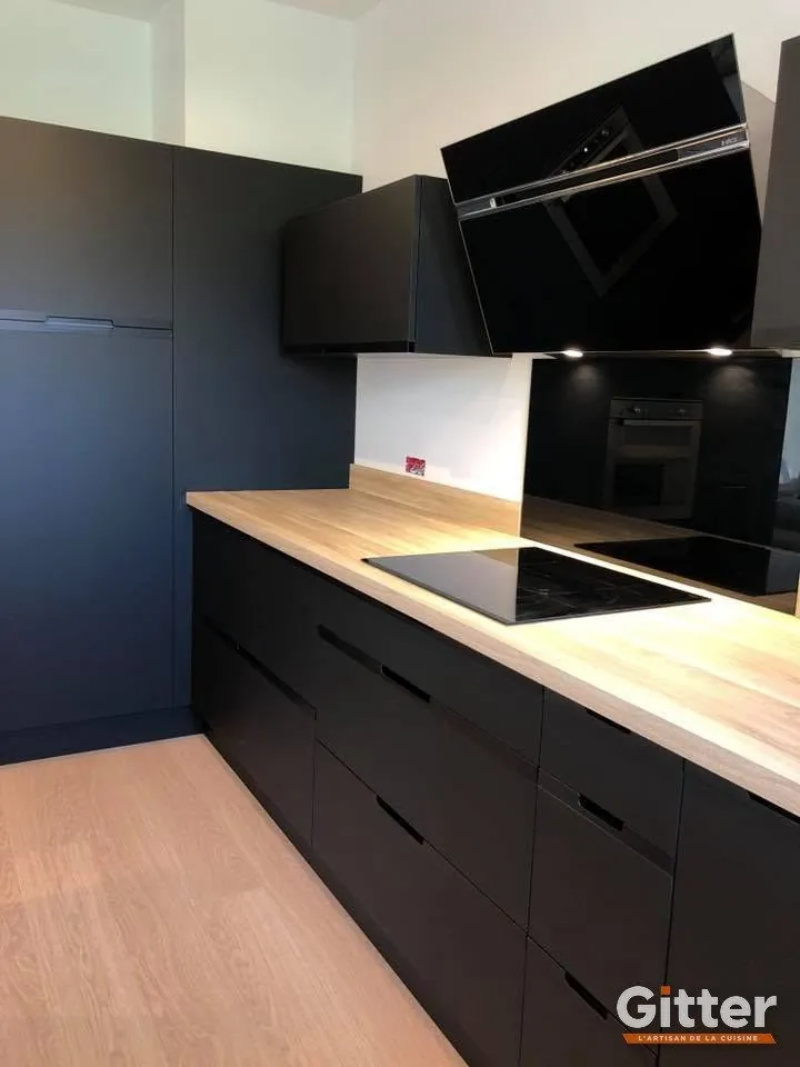 Cuisine : façades noires mates, plan de travail bois clair et hotte noire inclinée, réalisation Gitter à Fameck