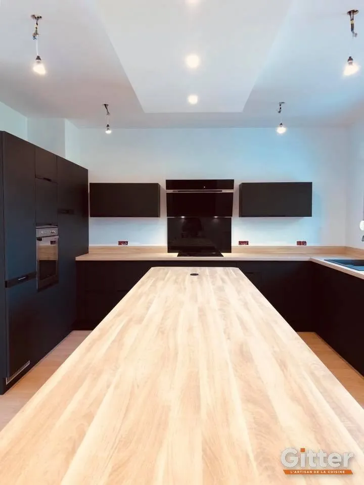 Cuisine : long îlot à plan de travail en bois, façades noires et éclairage en corniche, réalisation Gitter à Thionville